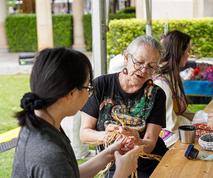 An Indigenous elder shows a UQ student a weaving technique