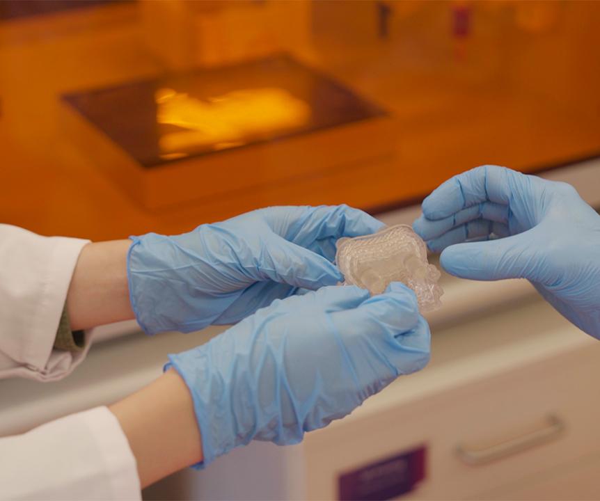 Researchers hold a clear plastic item, developed in a UQ research lab