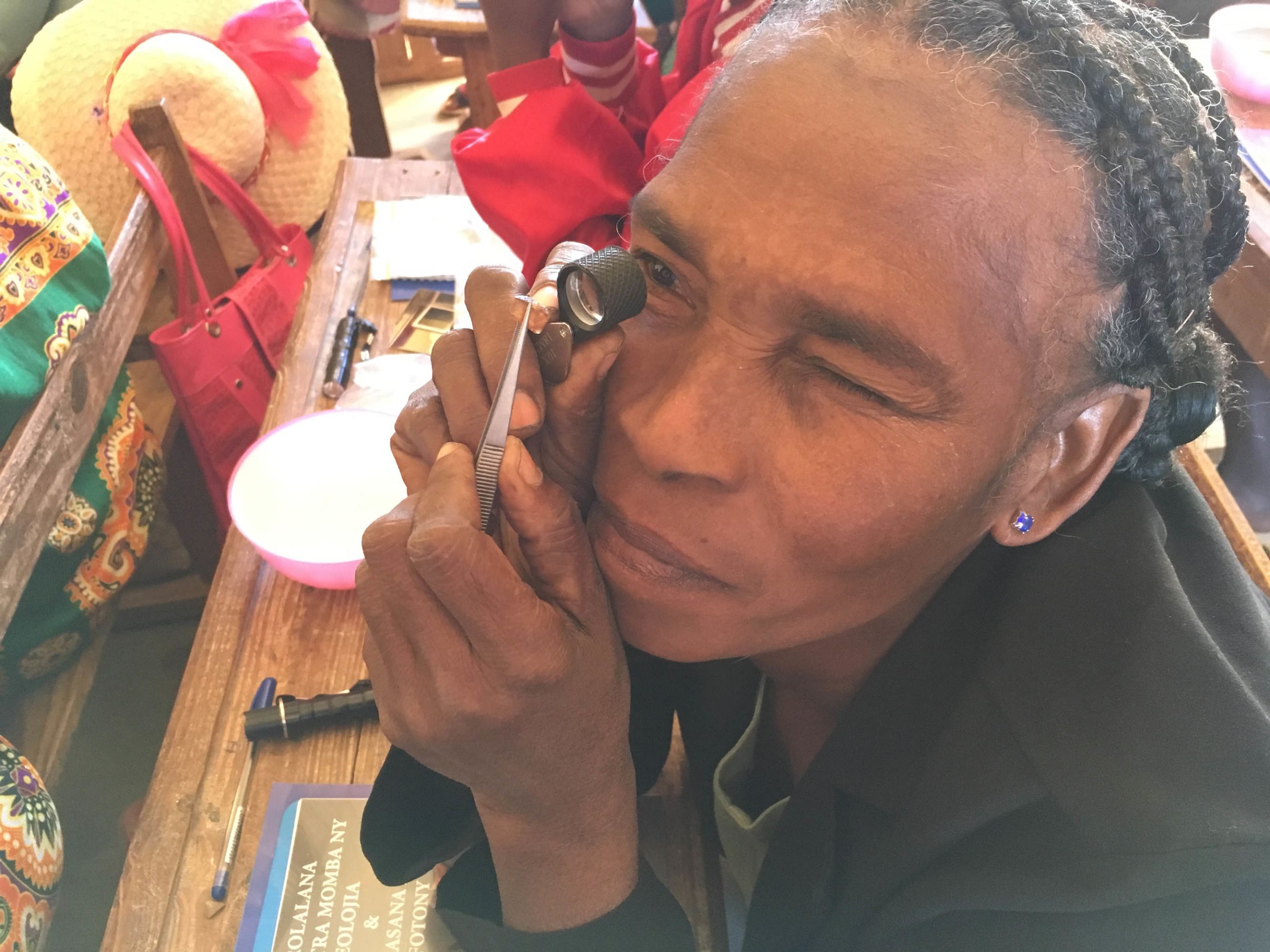 Malagasy sapphire miner learning to use loupe and tweezers to identify her stone
