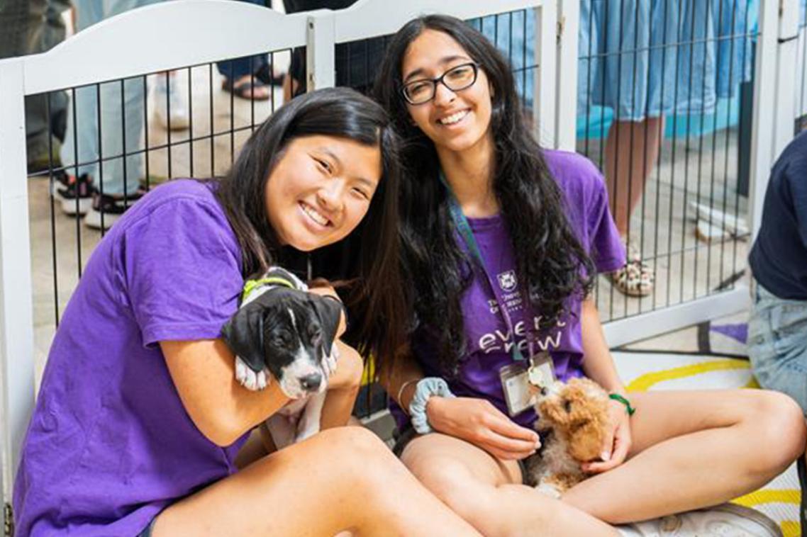 2 students smiling as they cuddle puppies.