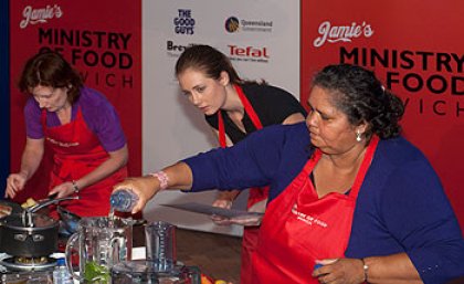 UQ student Charlotte Rashleigh assists Narrella Simpson, with Minister for Transport Rachel Nolan cooking in the background