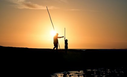 Silhouette of two people spear fishing 