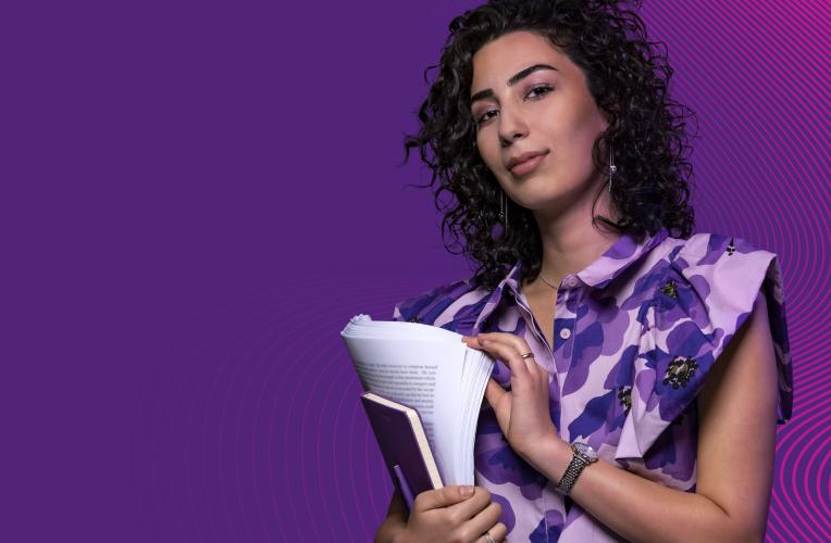 Woman in floral purple shirt holds a book and papers.