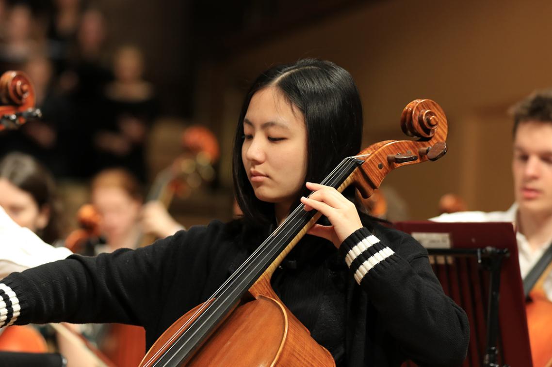 Student playing cello as part of an orchestra.