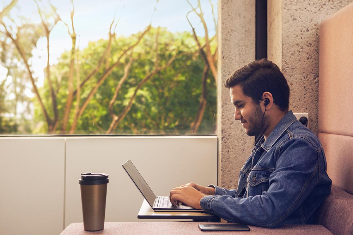 Student seated next to a window using a laptop while wearing headphones.