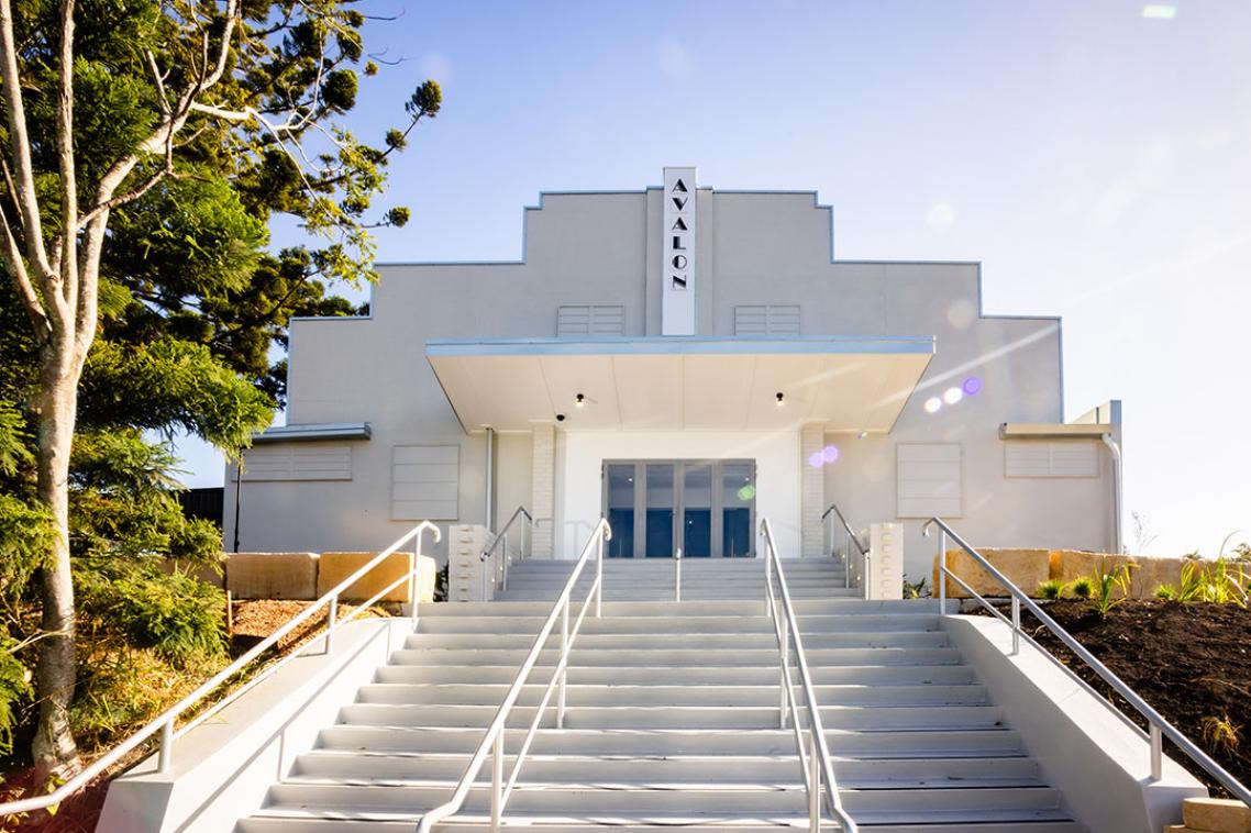 A white theatre with a sign on the roof that reads "avalon" 