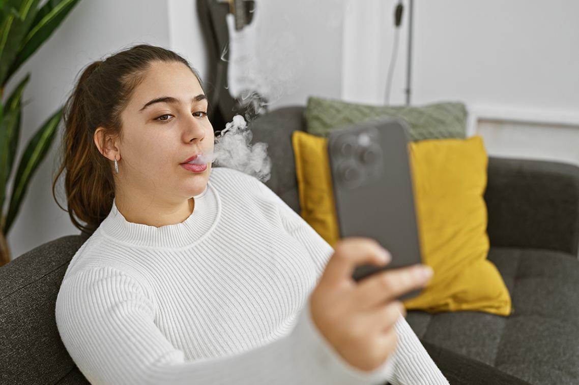 A woman taking a selfie on her mobile phone while blowing out a puff of smoke 