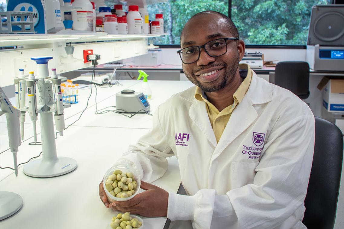 A man wearing a lab coat smiling at the camera while holding a small container of Kakadu plums